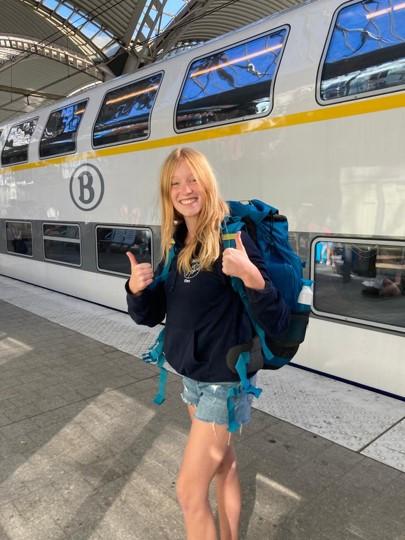 Fien lachend met de duimen omhoog in het station voor een trein van de NMBS