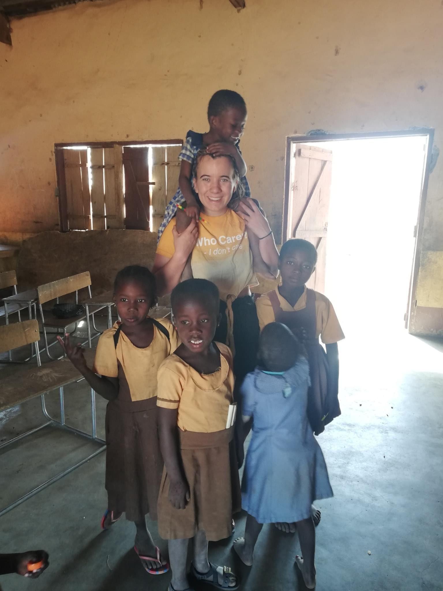 Melissa in een klaslokaaltje in Ghana met vier kindjes voor haar en een kindje in haar nek, poserend voor de foto