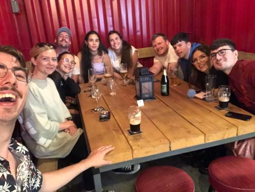 Willem neem een selfie met negen andere mensen. Iedereen lacht naar de camera. Ze zitten in een café rond een tafel met elk een drankje voor zicht.