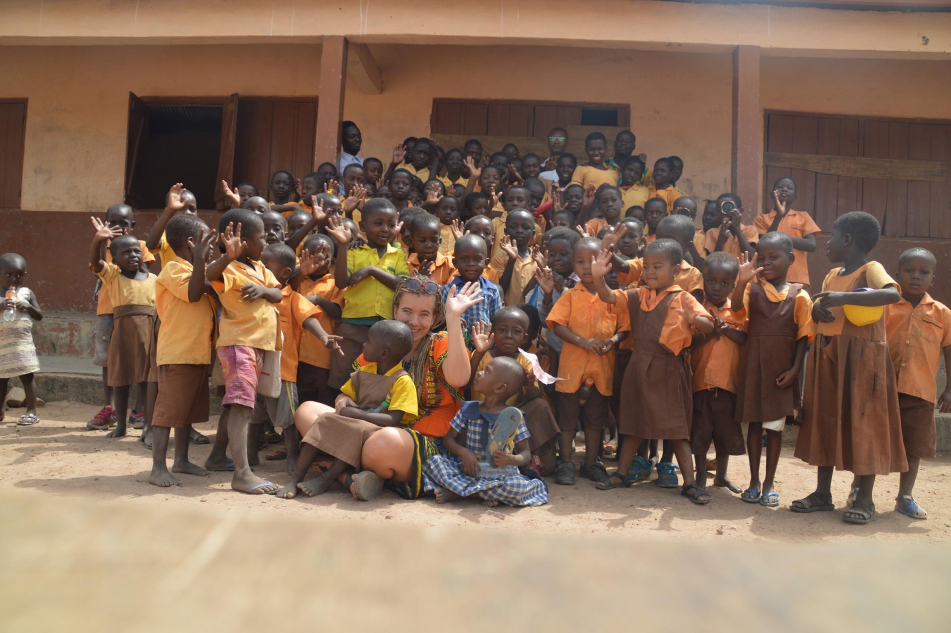 Een schoolfoto met zo'n vijftig kinderen poserend in hun geel-bruin uniform voor het schoolgebouwtje in aardekleuren. 