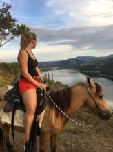 Emma zit op een paard en kijkt uit over het landschap. Er is water met daarrond bergen.