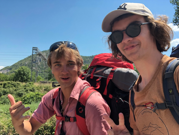 Mauro (rechts in de foto) neemt een selfie met een andere jongen. Ze lachen naar de camera. Ze dragen allebei een trekrugzak. Op de achtergrond is veel groen te zien met een berg.