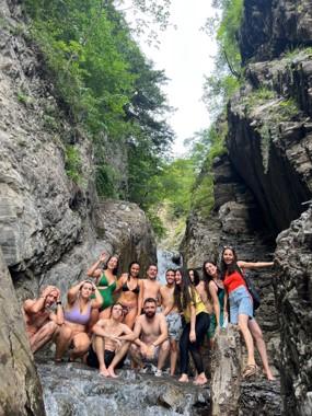 Een groep van ongeveer 12 jongeren in de natuur bij een waterval in badkledij
